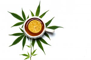 Cup of marijuana infused tea in a cup on top of marijuana leaves